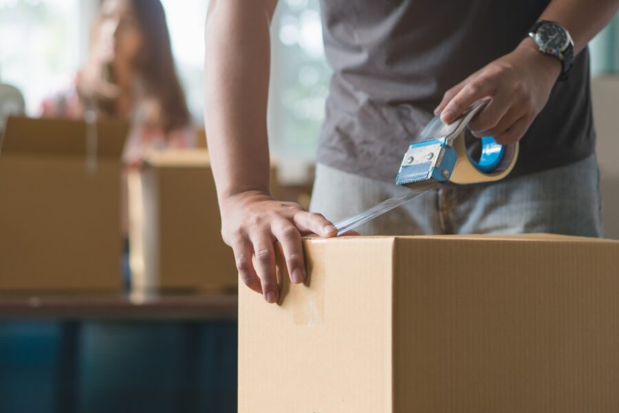 Concept Young Couple Moving House. Close Up Hand Of Man Use Tape Sealing Cardboard Box.