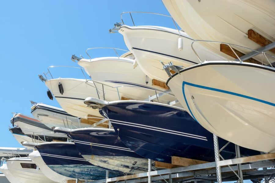 View From Below Of The Hulls Of Motorboats Racked One Above Another On Two Levels In A Dry Rack Boat Storage Facility Against Blue Sky.